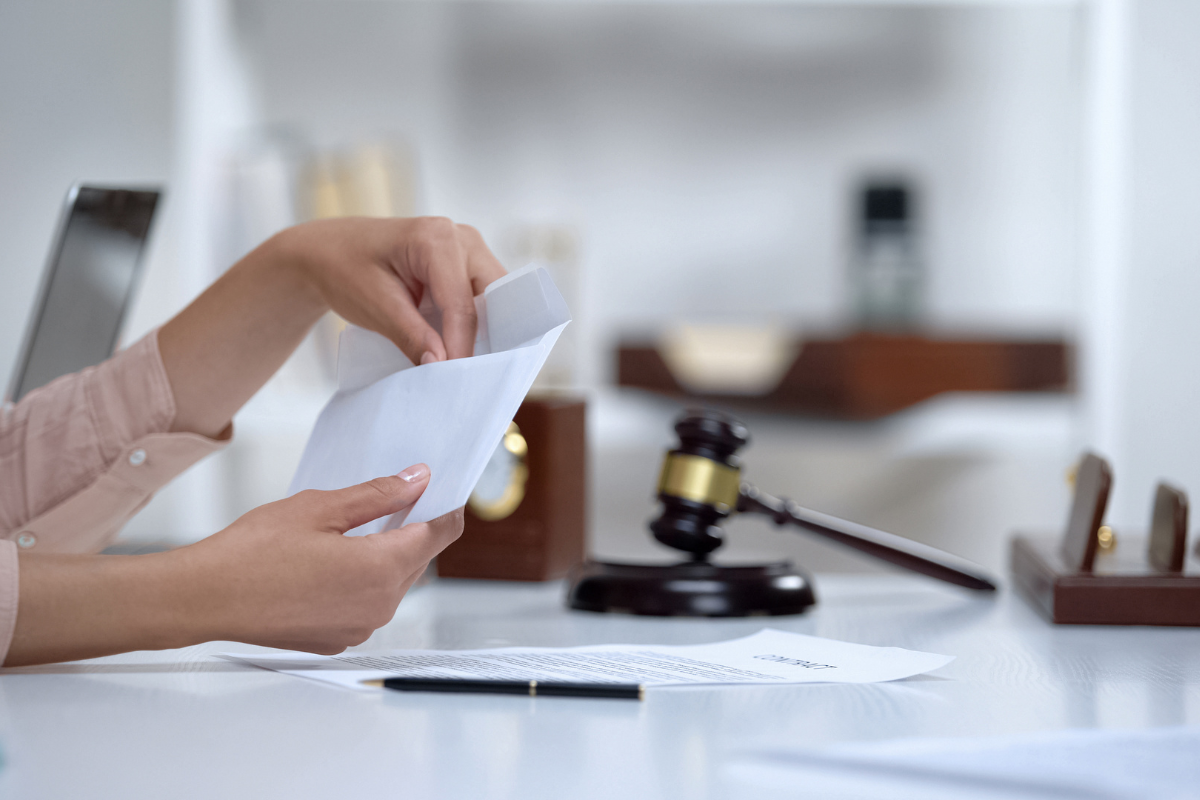 A woman is sitting at a lawyer's office with a gavel in the background, opening an envelope, which is presumed to be alimony money